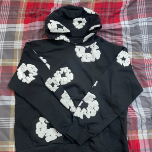 Svart hoodie Denim Tears - Svart hoodie från Denim Tears i storlek M med stora vita blommönster över hela tröjan. Tröjan har huva och ribbade muddar. Perfekt för dig som vill sticka ut med en unik och trendig streetwear-look.