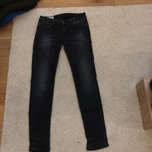 Svarta jeans från Dondup - Snygga svarta skinny jeans från Dondup med diskret slitning och klassiska fem fickor. Jeansen har en mörk tvätt, silverfärgade detaljer och läderpatch med logga bak. Perfekta för dig som gillar en tight passform och stilren look.
