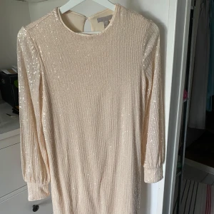 Champagnefärgad paljettklänning - Lite kortare än till knäna. Använd ett nyår. Klänningen har underklänning medans armarna endast är mesh.