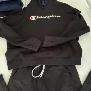 Svart Champion hoodie med logga - Svart hoodie från Champion i storlek XL med stor broderad Champion-logga i vitt och rött på bröstet. Klassisk huva och ribbade muddar vid ärmslut och nederkant. Perfekt för chill eller streetwear. Mjuk och skön bomullsmix som håller dig varm under höst och vinter.