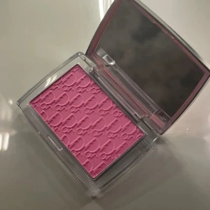 Dior Rosy Glow Rouge 001 Pink - Dior Rosy Glow i nyansen 001 Pink är ett puderrouge med ikoniskt Dior-mönster. Färgen är en intensiv, kall rosa som ger kinderna en fräsch och naturlig glow. Kommer i en lyxig transparent dosa med spegel, perfekt att ha i väskan för touch-ups. ENDAST TESTAD. 