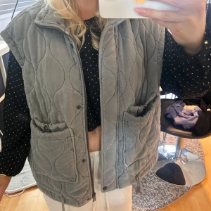 Grå quiltad väst  - Säljer en grå quiltad väst med fickor framtill och dragkedja från Zara. Västen har en loose fit och cool vågig quiltning som ger en trendig look