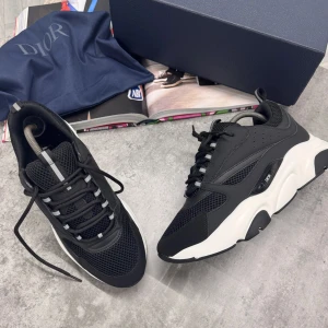 Svarta Dior B22 sneakers från Dior - Snygga Dior B22 sneakers från Dior i svart mesh och skinn med vita, kraftiga sulor. Skorna har rund tå, snörning och coola detaljer på sidorna. Perfekta för dig som vill sticka ut med en lyxig och modern look.