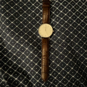 Klassisk klocka från Gant med läderband - Stilren klocka från Gant med rund, silverfärgad boett och ljus urtavla. Klockan har ett brunt läderarmband med krokodilpräglad yta och diskreta detaljer. Perfekt accessoar för dig som gillar en clean och tidlös look.