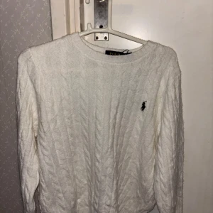 Vit kabelstickad tröja Polo Ralph Lauren - Vit kabelstickad tröja från Polo Ralph Lauren med klassisk rund halsringning och broderad logga på bröstet. Långärmad och i mjukt material som passar perfekt till jeans eller kjol. Enkel och stilren design som alltid funkar. Tag fås med, Qr Scan på tröjan finns
