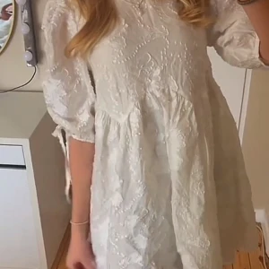 Vit blommig kortklänning & Other Stories - Supersöt vit kortklänning från & Other Stories med blommigt mönster i tyget. Klänningen har puffiga trekvartsärmar med knytband och en loose passform. Materialet är glansigt och känns lyxigt, perfekt för sommarens alla tillfällen. Klänningen är ny med prislapp kvar