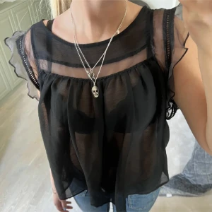 Svart transparent blus med volang - Säljer en svart, transparent blus med volangdetaljer på ärmarna och lös passform. Köpt här på plick (lånad bild) men först köpt från Mango. Bra skick. Ställ gärna frågor💕