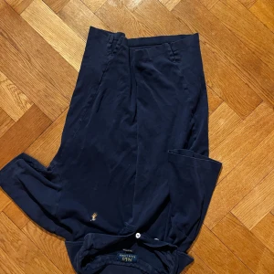 Mörkblå pikétröja från Polo Ralph Lauren - Klassisk mörkblå pikétröja från Polo Ralph Lauren med korta ärmar och vit knappslå. Ikoniska broderade loggan i gult på bröstet. 