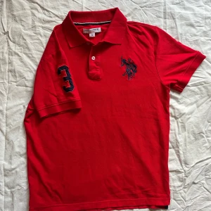 Röd polo t-shirt från U.S. Polo Assn. - Klassisk röd pikétröja från U.S. Polo Assn., herrstorlek S. Tillverkad av mjuk och slitstark bomull med sportiga detaljer: • Stor broderad logotyp på bröstet • Nummer 3 på höger ärm • Klassisk krage med knappslå  📏 Mått (platt): • Längd: ca 62 cm • Bröstvidd: ca 50 cm  Skick: Mycket bra – inga fläckar eller hål. Perfekt för både vardagsbruk och smarta casual-tillfällen.