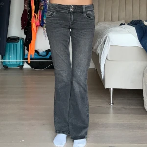 Grå bootcut jeans  - Snygga grå jeans från Gina Tricot i bootcut-modell. Jeansen har klassiska fickor fram och bak med lock och knapp på bakfickorna. De är tillverkade i ett mjukt denimtyg och har en mörkgrå tvätt. Jag är 172 och de passar i längen, midjan går att justera. Använda 2 ggr.