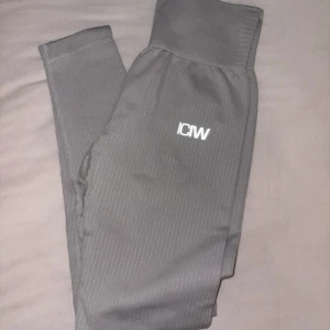 Grå ribbade leggings från ICANIWILL - Grå leggings från ICANIWILL med diskret ribbad struktur och hög midja. Snyggt broderad logga på låret. Tillverkade i stretchigt material med 92% nylon och 8% spandex för en tight och bekväm passform. Perfekta för träning eller chill.