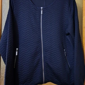 Mörkblå quiltad jacka med dragkedja - Snygg mörkblå jacka med quiltat sicksackmönster och silverfärgade dragkedjor framtill och vid fickorna. Jackan har rund halsringning och långa ärmar, perfekt för dig som gillar stilrena detaljer och en modern look.