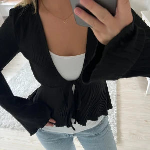 Svart blus med rosett - Superfin svart topp från Gina Tricot. Den har vida ärmar och snören där fram så att man kan knyta ihop den. Passar bra som festtopp men kan också användas till vardags!