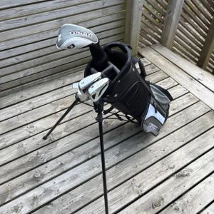 Junior golfbag från Open  - Det här är ingen bok, utan ett set med golfklubbor och en golfbag från märket Open. Perfekt för dig som vill börja spela golf eller behöver extra klubbor. Bagen har dock en trasig rem, se bild för detaljer.