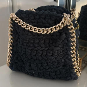 Mörkblå stickad axelväska - Säljer en mörkblå stickad axelväska med chunky guldfärgad kedja som axelrem och detaljer runt kanterna. Den är köpt av en tjej som stickar sådana väskor och säljer dem på Instagram. Säljer väskan då jag nästan aldrig använt den.