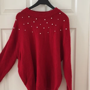 Röd stickad tröja med pärlor från H&M - Superfin röd stickad tröja med pärldetaljer över axlar och bröst. Tröjan har en rund halsringning och långa ärmar, perfekt för att liva upp din höst- eller vinterstil. Snygg att matcha med jeans eller kjol för en trendig look. Passar perfekt till Julen. 