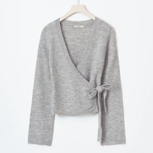 Grå omlottkofta med knyt - Supermjuk grå omlottkofta från Gina trico med v-ringning och knyt i sidan. Långärmad och i stickad kvalitet, perfekt för lager på lager. Enkel och stilren design som funkar till allt. Är i M men passar mig som har S och Xs i vanliga fall