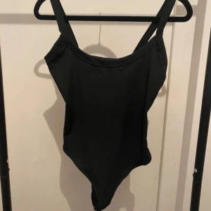 Svart ribbad body från SHEIN - Svart body från SHEIN i ribbat material med breda axelband och enkel, stilren design. Tillverkad i stretchig polyesterblandning som sitter snyggt på kroppen. Ihop sydd 