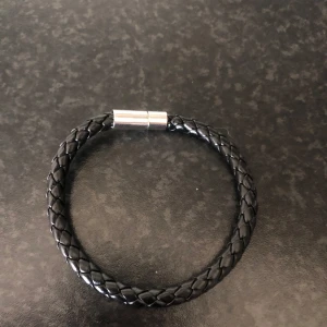 Svart flätat armband med metallspänne - Stilrent svart armband med flätad design och ett snyggt silverfärgat metallspänne. Perfekt accessoar för dig som gillar enkel men cool stil. Passar både tjejer och killar och är lätt att matcha med andra smycken. Kom med bud! Nypris 1200kr