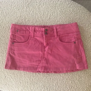 Rosa jeanskjol från Blanco, strl 36 - Säljer en snygg rosa jeanskjol från Blanco i storlek 36. Kjolen har klassisk femficksdesign, dubbla knappar framtill och bälteshällor. Baksidan har coola fickor med broderad detalj. Perfekt för dig som vill ha en färgstark och trendig look.