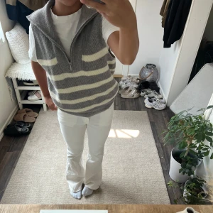 Gråvit randig stickad väst med half zip - Säljer en stickad väst i grått och vitt med breda horisontella ränder. Västen har en hög krage och en half zip-dragkedja framtill. Modellen är lite loose och passar perfekt över en t-shirt. Supermysig och trendig för lager-på-lager-stil.