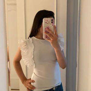 Vit topp med volangärmar från amisu - Supersöt vit topp från amisu/new yorker i storlek XS med breda volangärmar i transparent tyg och smockdetaljer längs axlarna. Toppens kropp är i mjuk bomullskänsla och har en figurnära passform. Perfekt för dig som vill sticka ut med en feminin och trendig look. Passar även till allt! Använd 1-2 gånger❤️