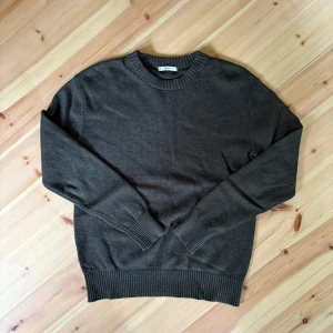 Mörkgrön stickad tröja  - En stilren mörkgrön stickad tröja med rund halsringning och ribbade muddar vid ärmslut och nederkant. Perfekt för lager-på-lager och passar till både jeans och chinos. Enkel och clean design som funkar året runt. 50% ull.