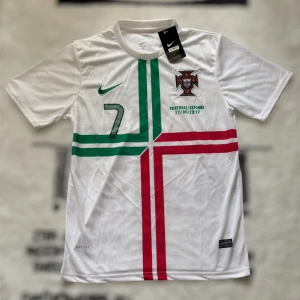 Portugal Ronaldo 7 fotbollströja Nike - Portugal fotbollströja från Nike med Ronaldo 7-tryck. Vit bas med gröna och röda korsade linjer på framsidan, broderat landslagsemblem och Dri-FIT-material. Kortärmad modell, perfekt för dig som älskar fotboll och vill sticka ut med en ikonisk tröja.