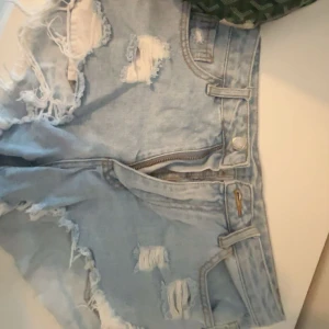 Ljusa jeansshorts - Snygga ljusblå korta jeansshorts med slitna detaljer och råa kanter. Klassisk femficksmodell med dragkedja och knapp framtill. Perfekta för sommaren och ger en avslappnad vibe till din outfit.