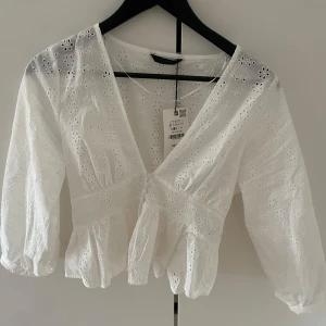 Vit broderad blus med v-ringning - Superfin vit blus från Zara med broderade blommor och v-ringning. Blusen har trekvartsärmar, knappar framtill och volang nedtill. Helt ny med prislapp kvar, säljer då den var för liten💕
