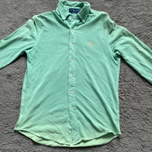 Mintgrön skjorta från Ralph Lauren  - Snygg mintgrön skjorta från Ralph Lauren i lätt och luftig bomull. Klassisk button-down krage, långa ärmar och knappar hela vägen. Ikoniska broderade polospelaren på bröstet. Perfekt för dig som gillar stilren och fräsch look. Retro
