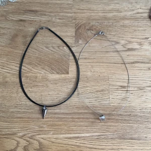 Två minimalistiska halsband med hängen - Säljer två stilrena halsband: ett med svart band och konformat silverhänge, och ett med tunn genomskinlig tråd och kubformat klart hänge. Perfekta för dig som gillar enkel och modern stil.