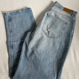 Ljusblå raka jeans från GinaTricot  - Säljer ett par ljusblå jeans från GinaTricot i storlek 38. Jeansen har raka ben, hög midja och stora slitningar över knäna och låret. 