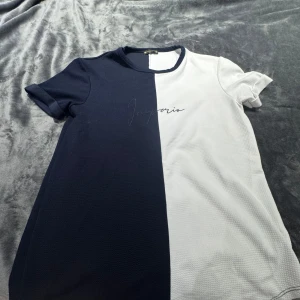 Tvåfärgad t-shirt från Imperio Cornetto - Snygg t-shirt från Imperio Cornetto i storlek XXL. Tröjan har en cool design med en rak delning i marinblått och vitt, samt diskret text på bröstet. Tillverkad i ett strukturerat tyg som känns skönt mot huden. Perfekt för dig som gillar stilrena kontraster.