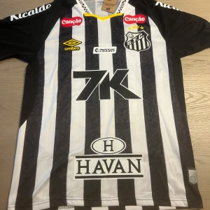 Santos FC Neymar Jr 10 matchtröja - Santos FC fotbollströja med Neymar Jr och nummer 10 på ryggen. Klassisk svartvit randig design, gula detaljer och flera sponsorloggor. Tillverkad i lätt och ventilerande material, perfekt för dig som älskar brasiliansk fotboll och vill sticka ut på planen.