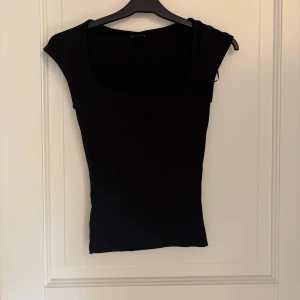 Svart topp med fyrkantig ringning Gina Tricot - Svart, tight topp från Gina Tricot med fyrkantig ringning. Sista bilden är bara för att visa hur den ser ut på. Den är svart och i storlek XXS men den är stretchig.