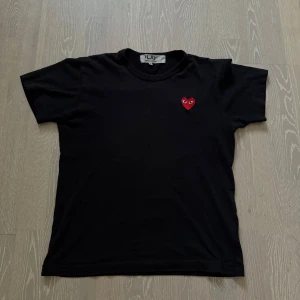 Svart Comme des Garçons Play t-shirt - Svart t-shirt från Comme des Garçons Play med klassiskt rött hjärta med ögon broderat på bröstet. T-shirten har rund hals, korta ärmar och är gjord i mjuk bomull. Hör av dig vid fler frågor eller funderingar 😁