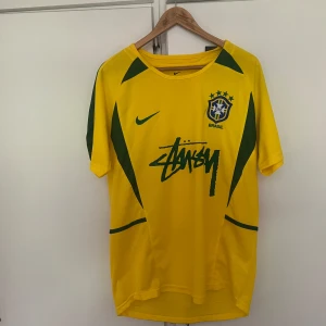 Brasilien x Stüssy x Nike fotbollströja M - Gul Brasilien fotbollströja i samarbete med Stüssy och Nike. Tröjan har gröna detaljer, CBF-emblem på bröstet och Stüssy-logga framtill. Tillverkad i lätt och ventilerande polyester med Dri-FIT-teknologi. Perfekt för dig som vill sticka ut på planen eller gatan. Pris kan diskuteras! 