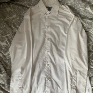 Vit skjorta - Klassisk vit skjorta med lång ärm och knappar framtill. Skjortan har en stilren krage och är gjord i bomull, perfekt för en clean och enkel look. Passar dig som gillar tidlös stil och vill ha något som funkar till många outfits. Säljer mycket skjortor så köp gärna flera i ett bundle!