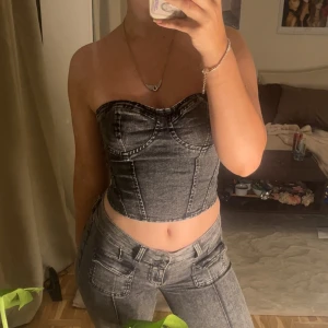 Grå jeanskorsett med dragkedja - Säljer en snygg grå korsettopp i jeansmaterial med markerade sömmar och croppad passform. Toppen är axelbandslös och har dragkedja i ryggen för enkel på- och avtagning. Perfekt för dig som vill ha en edgy och trendig look.
