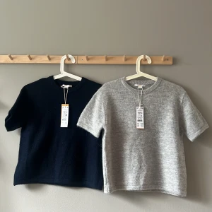 Stickad topp kort ärm grå & marinblå - Två stickade toppar med kort ärm i storlek 158/164. En i ljusgrå melange och en i marinblått, båda med rund halsringning och mjuk, mysig känsla. Perfekt för dig som gillar enkel och stilren look med en touch av cozy vibes.