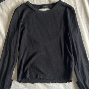 Svart ribbad topp med öppen rygg Gina Tricot - Svart långärmad topp från Gina Tricot i ribbad bomullsmix. Snygg detalj med öppen rygg och vågig kant nertill och vid ärmslut. Perfekt för dig som gillar stilrena plagg med en twist. Sitter tajt och passar till många olika looks.