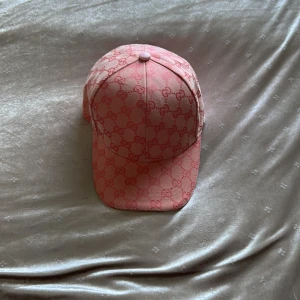 Rosa Gucci keps i merinoull - Exklusiv rosa keps från Gucci med ikoniskt GG-mönster över hela kepsen. Tillverkad i 90% merinoull och detaljerad med vit justerbar rem bak i skinn. Snygg och trendig accessoar som lyfter vilken outfit som helst.