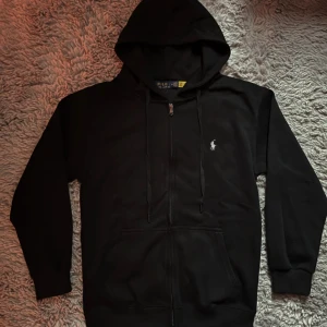 Svart hoodie från Polo Ralph Lauren - Svart hoodie från Polo Ralph Lauren med dragkedja, huva och snörning. Klassisk vit logga broderad på bröstet. Sprillans ny bara att köpa👍 Hör av dig vid intresse.