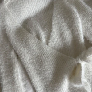 Vit fluffig omlottkofta med knyt - Supermjuk och fluffig vit omlottkofta med knyt i midjan. Koftan har lång ärm och är stickad i ett lurvigt material som känns extra mysigt. 💖