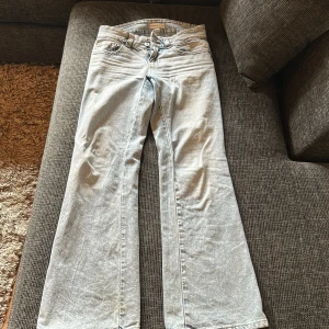 Ljusblå bootcut jeans med fickdetaljer - Snygga ljusblå jeans med bootcut passform och klassiska fem fickor, varav bakfickorna har lock och knapp. Jeansen har en ljus tvätt och är tillverkade i denim. Perfekta för dig som gillar en retro vibe och vill ha ett par jeans som sticker ut lite extra.