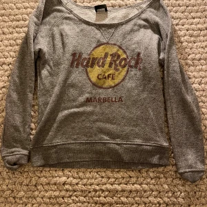 Grå Hard Rock Cafe tröja Marbella - Grå långärmad tröja från Hard Rock Cafe Marbella med klassiskt tryck i gult och rött framtill. Står ingen storlek men skulle gissa S/M