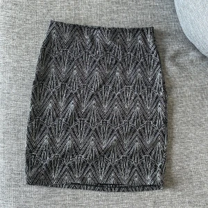 Glittrig svart minikjol från H&M Divided - Supersnygg svart kortkjol från H&M Divided i storlek XS. Kjolen har ett glittrigt geometriskt mönster i silver och är tillverkad i stretchigt material som sitter tight. Perfekt för dig som vill sticka ut med en cool och trendig look.