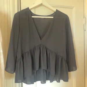 Svart volangblus med v-ringning - Supersöt svart blus från BikBok med v-ringning och volangdetaljer framtill. Lätt och luftig modell med trekvartsärm. 