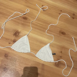 Vit triangelbikini - Supersöt vit triangelbikini från PrettyLittleThing med tunna knytband och lätt rynkade kanter. Klassisk modell med smala snören som knyts i nacken och ryggen. Perfekt för stranden eller poolen. Materialet är mjukt och följsamt syntet. Passar S/M.